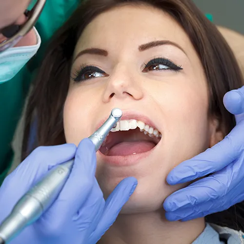 gloved hands using dental tool to clean woman's teeth