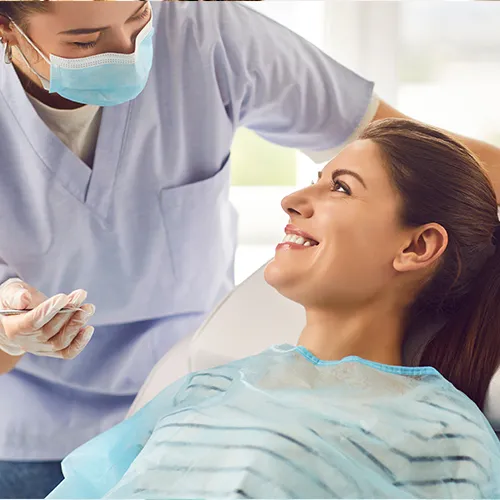 dentist wearing mask talking to smiling woman in dental chair