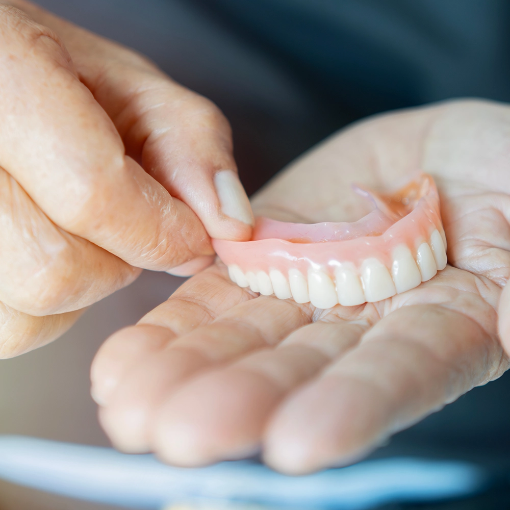 Close-up of a hand holding a lower denture, showcasing the detailed design and natural appearance of the artificial teeth.