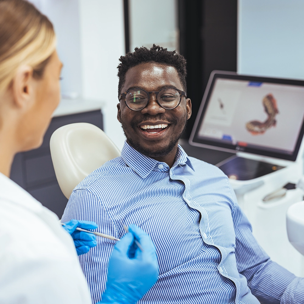 Male patient smiling while discussing dental treatments with a female dentist, highlighting a positive dental consultation experience.