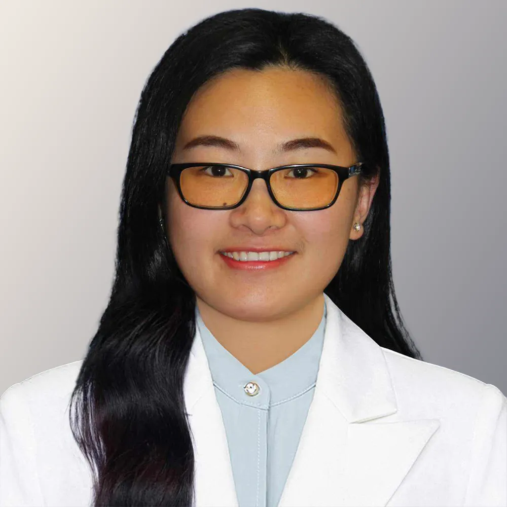 Portrait of Dr. Wang, a dentist wearing glasses and a white coat, smiling against a grey background.