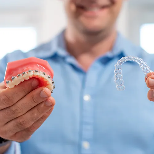 man holding braces model in one hand and clear aligner in the other hand